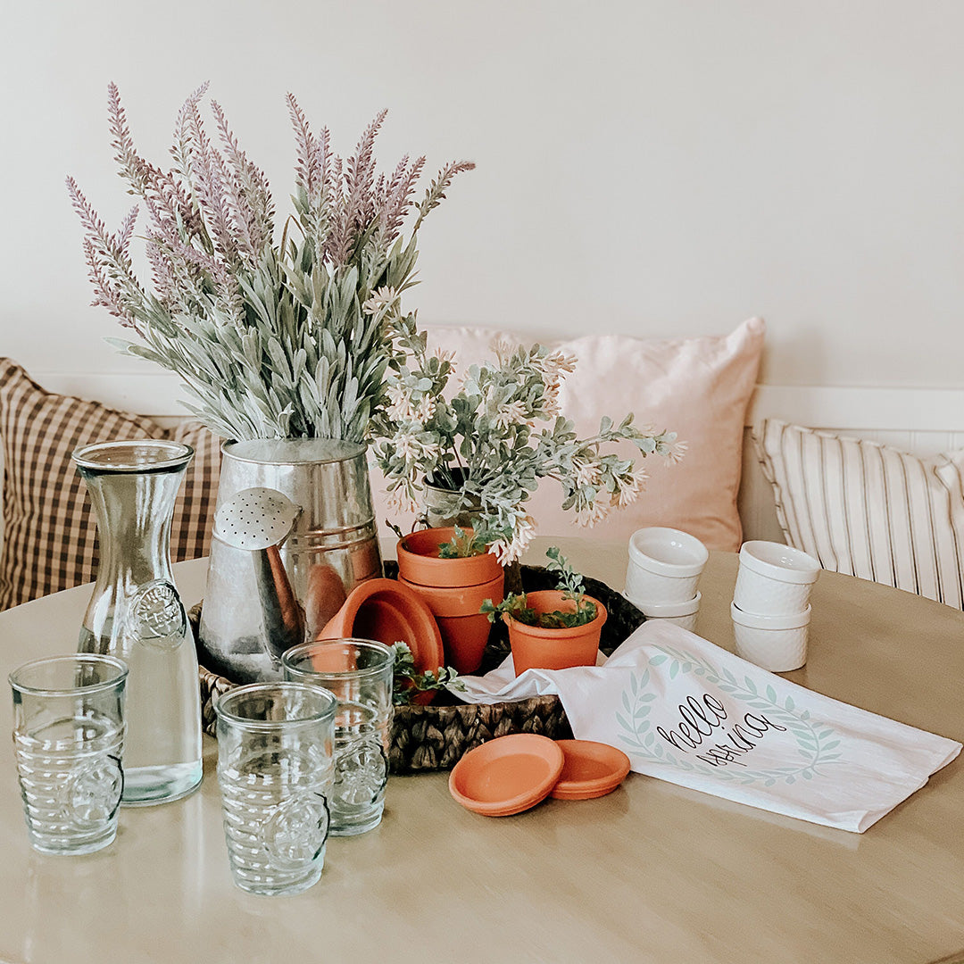 Breakfast nook topped with rustic decor including drinking glasses, a pitcher, terracotta planters, and a kitchen towel. 