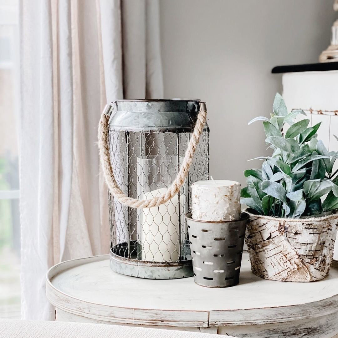 On a side table there is a rustic lantern, candle, planter, and faux greenery.