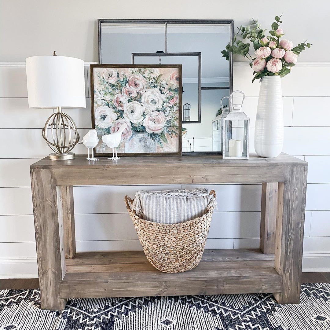 Entryway table with a lamp, wall decor, a vase, pink floral, and a wicker basket.